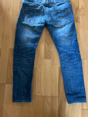Dondup Lucky 32 - Säljer ett par blå jeans från Dondup med snygga slitningar och tvättade detaljer. Jeansen har klassisk femficksmodell, knappgylf och raka ben. 