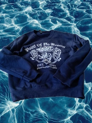 Mörkblå sweatshirt Piece of life - Mörkblå sweatshirt med tryck i vitt framtill där det står 'Point Of No Return' och 'EST. 2023'. Tröjan har rund halsringning, långa ärmar och ribbade muddar. Materialet känns mjukt och bekvämt, perfekt för en avslappnad stil.