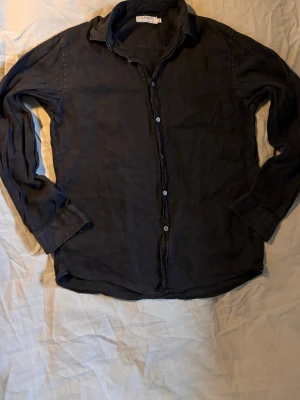 Svart linneskjorta från Ljung - Stilren svart skjorta från Ljung by Marcus Larsson i svalt linnematerial. Klassisk krage, långa ärmar och knäppning framtill. Perfekt för dig som gillar en enkel men snygg look.