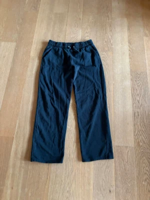 Svarta mjukisbyxor med dragsko - Säljer ett par svarta mjukisbyxor med bred resår i midjan och dragsko för skön passform. Byxorna har raka ben och är tillverkade i mjukt, bekvämt material. Perfekta för chill dagar eller när du vill ha det extra bekvämt.