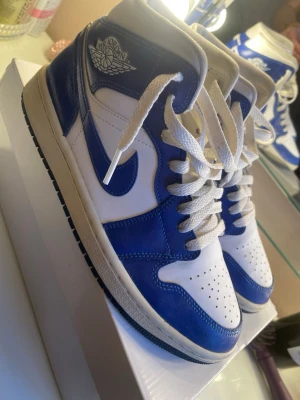 Air Jordan 1 Retro High kentucky blue - Säljer ett par Air Jordan 1 Retro High sneakers i blått och vitt läder. Klassisk high-top siluett med vita skosnören, blå yttersula och ikoniska Air Jordan-loggan på sidan. Perfekta för dig som vill sticka ut med en tidlös och sportig look.