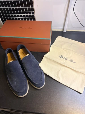 Blå mocka loafers från Loro Piana - Snygga loafers i blå mocka från Loro Piana med klassisk slip-on design och ljus sula. Skorna har en stilren och tidlös look, perfekt för dig som gillar exklusiva detaljer och hög kvalitet. Kommer med originalkartong och dustbag.