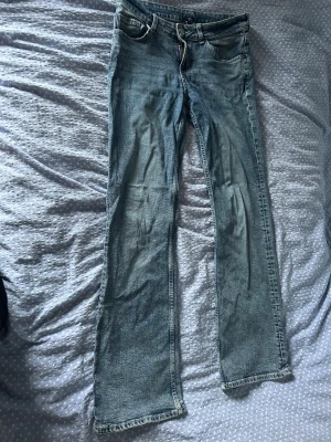 Ljusblå bootcut jeans - Säljer ett par ljusblå bootcut jeans med klassisk femficksdesign och dragkedjegylf. Jeansen har en lätt tvättad look och raka ben som slutar i en lätt utsvängd passform. Perfekta för en avslappnad och trendig stil.