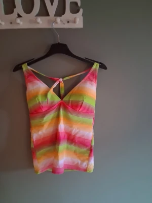 Färgglad randig badtopp💕 - Snygg linnetopp med färgglada ränder i rosa, grön, gul och vit. Toppen har smala axelband och en knytning framtill som ger en unik detalj. Perfekt för varma dagar och somriga outfits. Fodrade kupor💕
