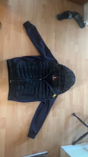 Mörkblå cardigan jacka från Parajumpers - Snygg mörkblå pufferjacka från Parajumpers med huva och hel dragkedja. Jackan har quiltad framsida och två sidofickor med dragkedja. Klassisk gul detalj vid kragen och ribbade muddar vid ärmslut. Perfekt för kyliga dagar.Ej använd jättemycket. Storlek M-L ‼️pris ej hugget i sten ‼️