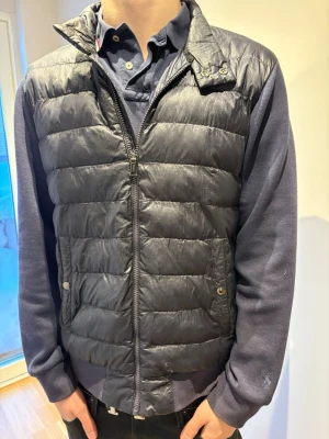 Polo Ralph Lauren Mörkblå Cardigan storlek M - Snygg mörkblå cardigan med quiltad design. Jackan har dragkedja framtill och två fickor med knappstängning. Perfekt att slänga en hoodie eller tröja under för extra värme. Klassisk och stilren look som funkar till det mesta. OBS liten defekt framtill. Hör av dig vid funderingar.
