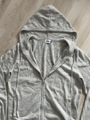 Ljusgrå kashmir zip hoodie från Don - Ljusgrå hoodie med dragkedja från Don. Klassisk modell med huva och dragsnören, samt fickor på sidorna. Tillverkad i mjukt och tunt material som känns skönt mot huden. Perfekt för en avslappnad och stilren look. Den är gjord av kashmir och bomull. 