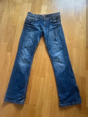 Blå bootcut jeans med broderade fickor - Snygga blå bootcut jeans med slitningar och broderade detaljer på bakfickorna. Jeansen har klassisk femficksdesign och lätt tvättad look. Perfekta för en avslappnad och trendig stil.