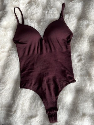 Vinröd body med tunna axelband - Snygg populär vinröd body med tunna justerbara axelband och vadderade kupor. Slutsåld och endast använd 1 gång🩷 Bodyn har en djup urringning och är tillverkad i ett mjukt, stretchigt material som sitter skönt mot kroppen. Perfekt att styla under en skjorta eller kavaj.