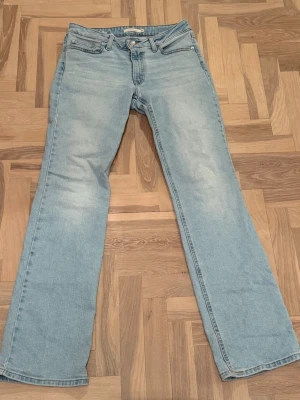 Levis Ljusblå raka jeans - Säljer ett par ljusblå Levis jeans med rak passform och klassisk femficksdesign. Jeansen har en något utsvängd benslut och subtila slitningar framtill. Perfekta för en avslappnad och trendig look.
