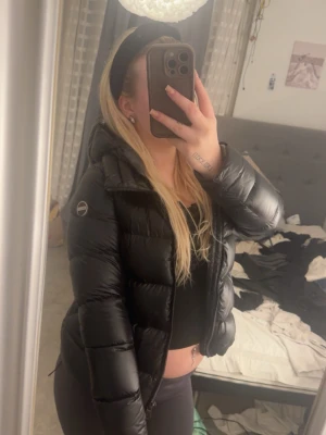 Svart pufferjacka med huva - Säljer en svart pufferjacka från colmar med huva och dragkedja framtill. Jackan har ett quiltat mönster och logotyp på ärmen. Perfekt för kalla dagar, passar till nästan alla outfits. köpt för 3200kr säljer för 1600kr använt två gånger.
