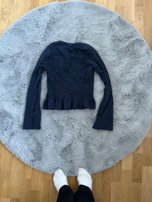 Mörkblå långärmad topp med volang - Säljer en mörkblå långärmad topp med smockad midja och volangkant nedtill. Toppen har en figurnära passform och är perfekt för dig som gillar en enkel men söt stil. Materialet känns mjukt och stretchigt.