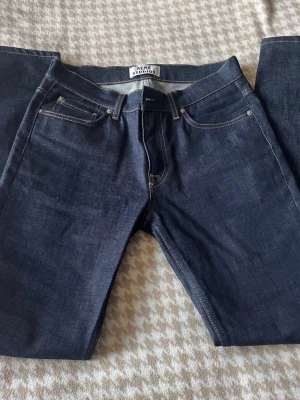 Mörkblå jeans från Acne Studios 31/32 - Snygga mörkblå jeans från Acne Studios med klassisk femficksmodell och raka ben. Jeansen har kontrastsömmar och är tillverkade i ett kraftigt denimtyg som ger en stilren och tidlös look. Perfekta för dig som gillar minimalistisk och modern stil. Ny pris är 4000 kr