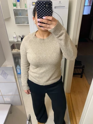 Beige stickad tröja med rund hals - En enkel och stilren beige stickad tröja med rund hals och långa ärmar. Tröjan har ribbade muddar vid ärmslut och nederkant, perfekt för att hålla värmen. Passar till både jeans och mjukisbyxor för en avslappnad look.