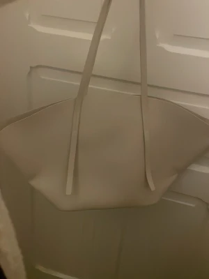 Beige shoppingväska i minimalistisk stil - Stilren shoppingväska i beige med långa axelband och rymligt huvudfack. Väskan har en enkel, modern design och är tillverkad i ett slätt material som känns mjukt. Perfekt för dig som gillar minimalistiska accessoarer och vill ha plats för allt du behöver.