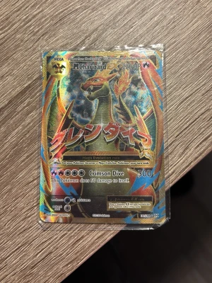 Pokémonkort Mega Charizard EX - Säljer ett samlarkort från Pokémon, Mega Charizard EX med holografisk yta. Kortet har färger i guld, blått, rött och svart och text på både engelska och japanska. Perfekt för dig som gillar Pokémon och vill utöka din samling.