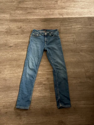 Blå raka jeans från Tommy Hilfiger - Snygga blå jeans från Tommy Hilfiger med klassisk femficksmodell och raka ben. Jeansen har en ljus tvätt och subtila slitningar för en avslappnad look. Tillverkade i bomull med en liten logga på bakfickan och patch med varumärket i midjan.slimfitt.