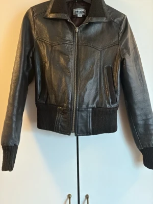 Svart skinnjacka från Mission - Snygg svart skinnjacka från Mission med klassisk krage, ribbade muddar och midja. Jackan har dragkedja framtill och två snedställda fickor. Perfekt för dig som vill ha en tidlös och cool look.