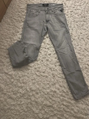 Grå jeans från Replay Anbass - Snygga grå jeans från Replay, modell Anbass (slim fit) . Klassisk femficksdesign med dragkedjegylf och raka ben. Jeansen har diskreta sömmar och är tillverkade i mjuk denim som ger en skön passform. Perfekta för en avslappnad stil.