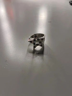 Silvrig ring med stjärndesign - Cool silvrig ring med en öppen design och en stor stjärna framtill. Ringen har små klara stenar infällda i stjärnan som ger extra bling. Passar perfekt för dig som gillar unika accessoarer med lite edge. Justerbar storlek för bästa passform.