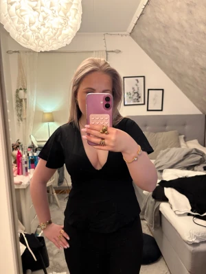 Svart blus med v-ringning - Svart blus med v-ringad hals, knytning i ryggen och korta ärmar ger en snygg och feminin siluett. Perfekt för dig som gillar stilrena och klassiska toppar.