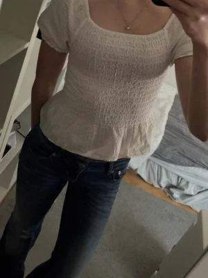 Vit smockad blus med puffärm - Supersöt vit topp/blus med smockat tyg och puffiga korta ärmar. Använd ett fåtal gånger. Köpt på Kappahls barnavdelning i storlek 158/164 men motsvarar XS