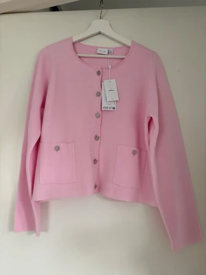 Ljusrosa kofta från Vila oanvänd  - Supersöt ljusrosa kofta från Vila med rund halsringning och knappar framtill. Koftan har två fickor framtill och är tillverkad i ett mjukt stickat material. Perfekt för lager-på-lager och en chill look. Oanvänd strl xl men passar även m-l