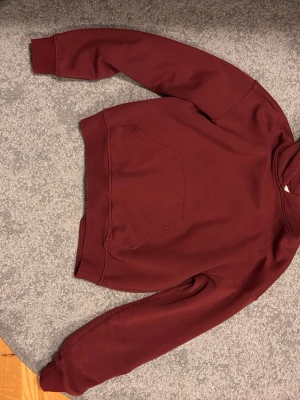 Vinröd hoodie från Gina tricot - Mysig vinröd hoodie från Gina tricot i storlek XXS. Klassisk modell med huva och stor magficka framtill. Tillverkad i mjukt bomullsmaterial som känns skönt mot huden. Perfekt för chill dagar eller när du vill ha en enkel och snygg look.