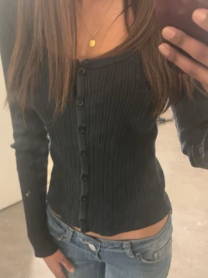 Svart ribbad tröja från Brandy Melville - Säljer en svart ribbad tröja från Brandy Melville med lång ärm och knäppning framtill. Den är urringad och har stretchigt material.