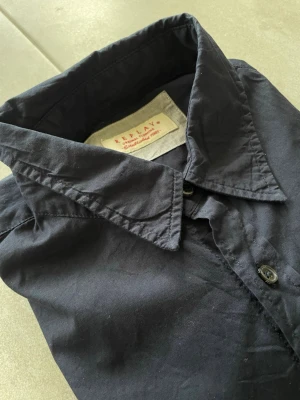 Mörkblå skjorta från Replay - Klassisk mörkblå skjorta från Replay med knappar framtill och lång ärm. Skjortan har en stilren design med liten broderad detalj på bröstet och normal passform. Perfekt till jeans eller chinos för en clean look.