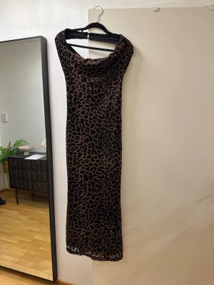 Leopardmönstrad långklänning - Snygg långklänning med leopardmönster i svart och brun. Klänningen har en lösare passform upptill med bred urringning och är ärmlös. Materialet känns mjukt och stretchigt, perfekt för dig som vill sticka ut.