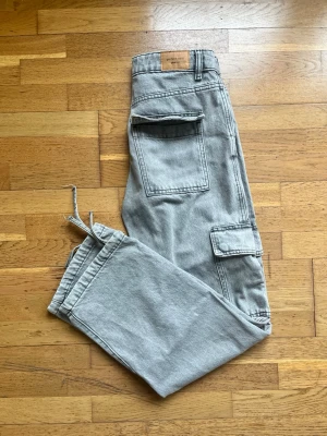 Grå cargobyxor från Perfect Jeans - Säljer ett par grå cargobyxor från Perfect Jeans med klassiska stora fickor på sidorna och en cool, avslappnad passform. Byxorna har dragkedja och knapp framtill samt hällor för bälte. Materialet är slitstark denim som ger en snygg look.