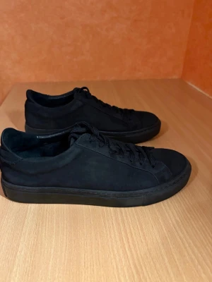Garment Project mockaskor - Ett par svarta skor från Garment Project i nubuck-läder, storlek 40.  Skorna är väldigt varsamt använda och i princip nyskick. Enda anmärkningen är ett litet snitt vid hälen (vänster sko), syns knappt i verkligheten (se bild).  Butikspris 1800kr  Material: • Överdel: 100% nubuck • Foder/övre foder: 100% läder