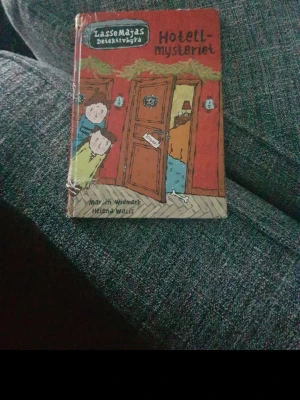 LasseMajas Detektivbyrå: Hotellmysteriet - En illustrerad bok ur serien LasseMajas Detektivbyrå, 'Hotellmysteriet', skriven av Martin Widmark och illustrerad av Helena Willis. Omslaget är färgglatt med tecknade figurer och dörrar i ett hotell. Perfekt för unga deckarfans.