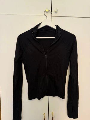 Svart ziptröja med hög krage - Säljer en svart ziptröja med hög krage och långa ärmar. Tröjan har en smal passform och dragkedja framtill. Perfekt för lager på lager och enkel att matcha med olika outfits. Perfekt att ha på långpromenad eller vägen till träning. Ganska liten i storleken