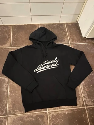 Saint Laurent hoodie - Riktigt fet och eftertraktad hoodie med saint laurent loggan. Storlek S, skick 10/10!! Saknar lapp i nacken så är lite osäker på äktheten så därför är priset just nu på 999kr! Nypris runt 7000! Tveka inte med att ställa frågor!
