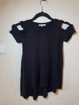 Svart topp med öppna axlar Superdry - Snygg svart topp från Copper Key med korta ärmar och trendiga öppna axlar. Toppen har volangdetaljer vid axlarna och är gjord i mjuk bomull. Perfekt för dig som vill ha en enkel men ändå unik look. Fint skick, inga skavanker. Copper Key, storlek S. Djur, rök och parfymfritt hem.