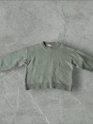 Grön stickad tröja med pärlor - Snygg grön stickad tröja med rund hals och dekorativa pärlor över hela framsidan och ärmarna. Tröjan har ribbade muddar vid ärmslut och nederkant, vilket ger en skön och avslappnad passform. Perfekt för dig som vill ha något extra i vardagen.