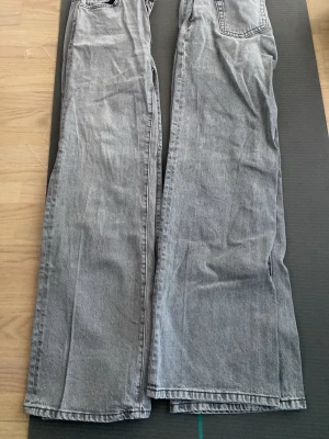 Gråa vida jeans med raka ben - Säljer ett par gråa jeans med breda, raka ben och klassiska fickor både fram och bak. Jeansen har en avslappnad passform och är perfekta för en trendig och chill look. Materialet är denim i bomull och färgen är tvättad grå. Båda är exakt likadana.