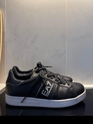 EA7 Emporio Armani sneakers  - EA7 Emporio Armani sneakers i svart. Använda ca 4–5 gånger.  Skorna är i fint skick. Sulan har normala spår av användning undertill och det finns någon enstaka liten fläck på utsidan, inget som syns tydligt när de används. Säljs pga kommer inte till användning. 
