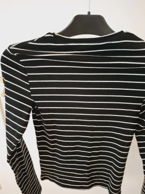 Svartvit randig långärmad topp - Snygg svart långärmad topp med vita horisontella ränder. Figurnära passform och klassisk rund halsringning. Perfekt att styla med jeans eller kjol för en clean och trendig look.