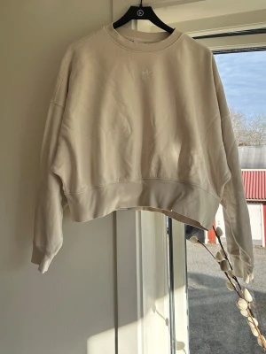 Beige cropped sweatshirt från Adidas - Säljer en beige cropped sweatshirt från Adidas med diskret logga broderad framtill. Tröjan har rund halsringning, långa ärmar och avslappnad passform.🤎