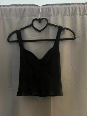 Svart ribbad croppad topp - Snygg svart croppad topp med breda axelband och ribbad struktur. Enkel och stilren design som passar till många outfits.