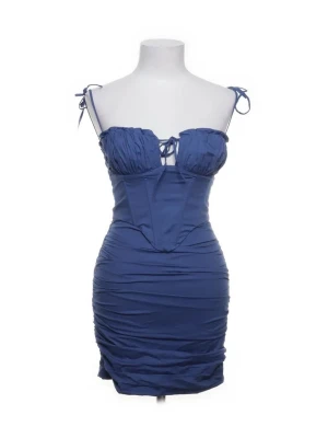Oh polly klänning - Snygg blå kort klänning med smala axelband som knyts och snörningsdetalj framtill. Klänningen har figurnära passform och rynkade detaljer längs sidorna för en trendig look. Perfekt för sommarens alla tillfällen.