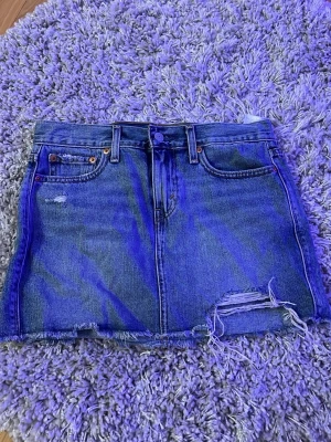 Blå jeanskjol från Levi's - Säljer en blå jeanskjol från Levi's med slitna detaljer i storlek 24