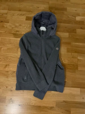 Unik grå Moncler cardigan  - Säljer en grå stickad jacka från Moncler med vadderad huva och dragkedja framtill. Jackan har ribbade muddar, två fickor med dragkedja och Moncler-logga på ärmen. Perfekt för kyliga dagar och riktigt snygg till jeans. Priset är ej hugget i sten‼️