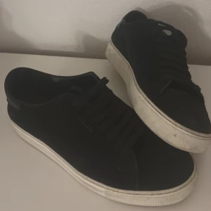 Svarta sneakers från Axel Arigato - Stilrena svarta sneakers från Axel Arigato med lågt skaft och vita sulor. Skorna har en minimalistisk design med diskret logga på sidan och är tillverkade i mocka. Perfekta för en clean och modern look. Skorna är hela , inte sönder men kan behövas tvättas , skorna är i storlek 38 superbekväma och säljs för 1430 kr