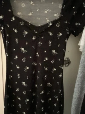 Svart blommig kortklänning - Söt svart kortklänning med små vita blommor och v-ringad hals. Klänningen har korta ärmar och en figurnära passform. Helt ny