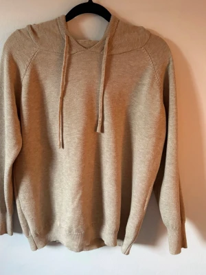 Beige merinoull hoodie  - Mysig beige stickad hoodie med huva och dragsnören. Perfekt för dig som gillar en enkel och stilren look. Materialet känns mjukt och skönt mot huden. 