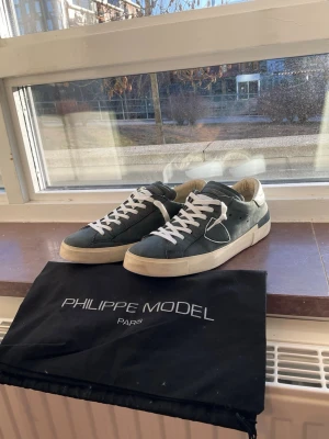 Philippe Model blåa sneakers - Snygga blåa Philippe Model skor med vita detaljer och vita skosnören. Klassisk låg modell med vit sula och diskret logga på sidan. Kommer med original dustbag från Philippe Model Paris. Storlek 42 och i väldigt fint skick.